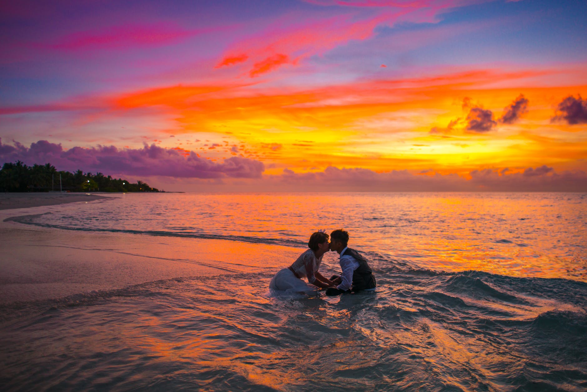 man and woman kissing in the ocean during sunset